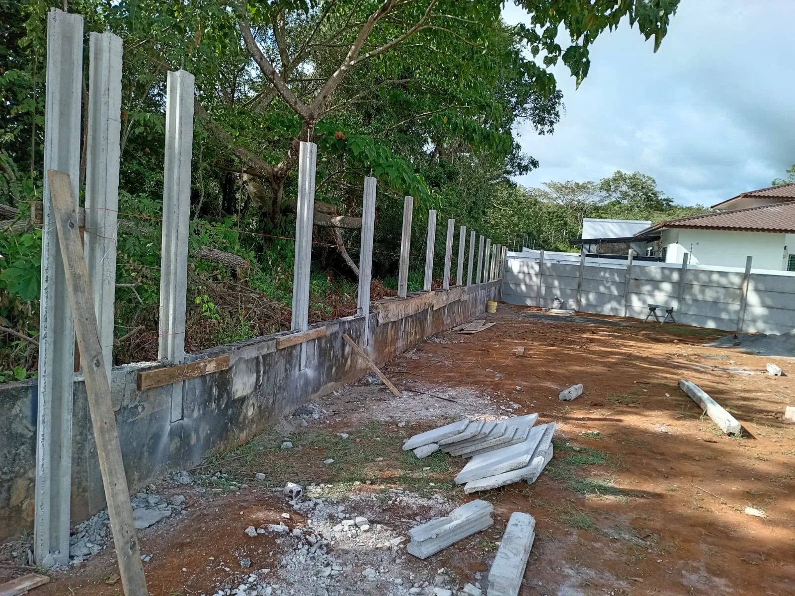 Columnas iniciales de muro perimetral con base de concreto y residencia con jardín al fondo